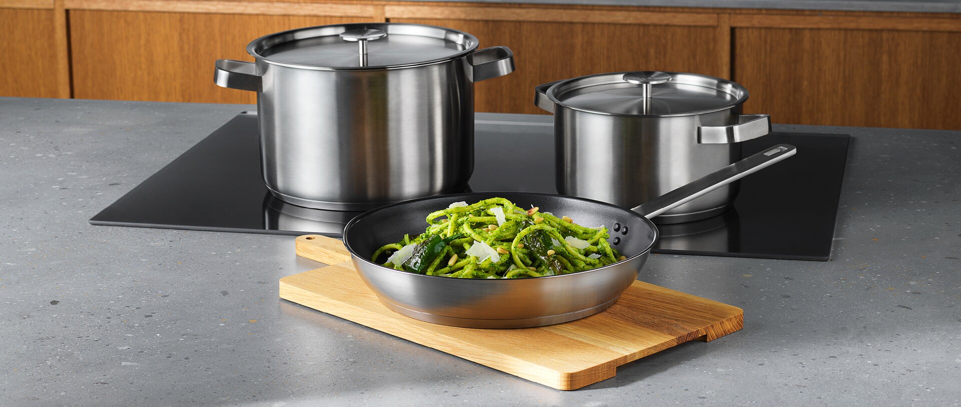 Un plan de travail avec une plaque à induction Electrolux sur laquelle sont posées deux casseroles et une planche à découper avec une casserole remplie d'aliments.